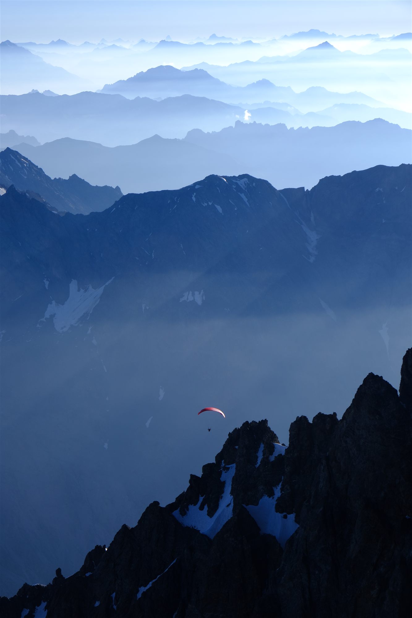 Un parapente rouge au-dessus de crêtes bleutées